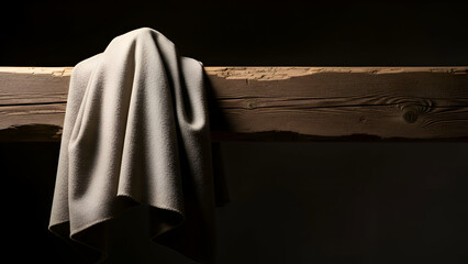 Fabric drapes over rough wooden beam in dimly lit room, creating a sense of mystery and anticipation with its soft folds and shadows.