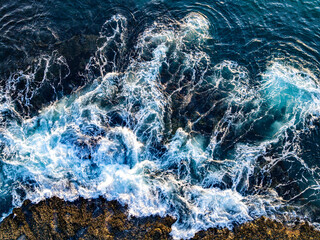 Turquoise sea water with reef. Ocean surf. Dramatic sea waves on reef. Coastal rocks and sea surf. Aerial view of ocean waves. Sea surface. Drone shot of beauty rocky coastline.
