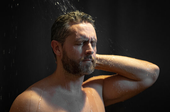 Man taking a shower and washing his face with soap. Mature male in the bath. Guy applying shampoo and foam to his hair in the bathroom. Man washing body and face in a modern bathtub.