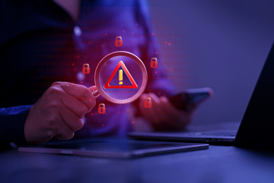 Cybersecurity threat detection concept. A hand holding magnifying glass with digital warning icon for data risk, cyber attack detection, system vulnerability, digital security analysis. digital alert.