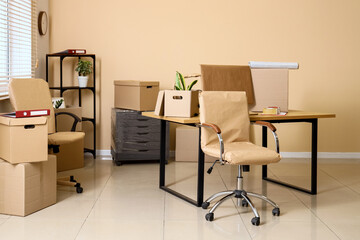 Desk with chairs and cardboard boxes in office on moving day