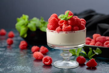 Panna cotta with fresh raspberries in a clear bowl.