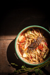 Thai spicy papaya salad with field crab served in a vintage enamel bowl on rustic wooden table, showcasing traditional flavors and authentic street food style.