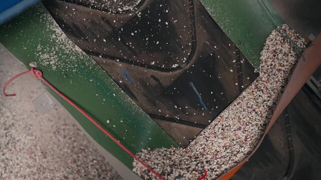 Processed rubber granulate flowing along conveyor inside recycling factory