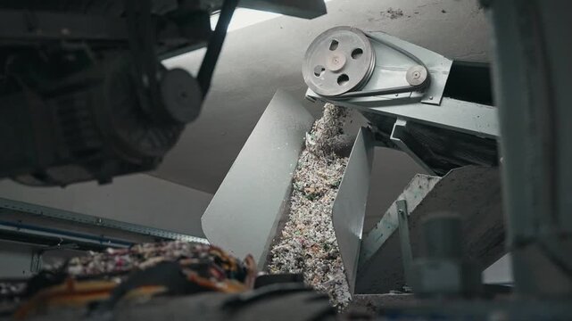 shredded rubber falling through metal chute in industrial recycling facility