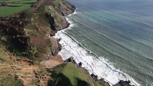 Side angle aerial movement over Pobbles Bay with cliffs beach and ocean unfolding along the Gower Peninsula coast in Wales