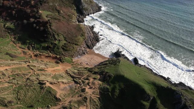 Drone rising and pulling away from Pobbles Bay with expanding views of the open sea and dramatic coastline in Wales