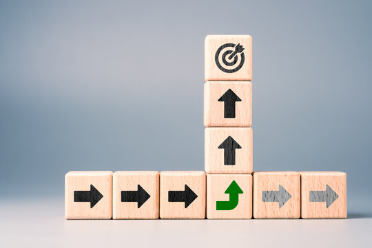Wooden blocks showing pivot strategy with a green arrow changing direction to reach the target representing goal shift, breakthrough, and strategic decision