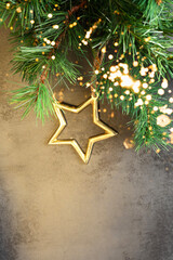 Golden Christmas star ornamnet hanging from a fir branch on black concrete background, Winter holiday greeting card, design with copy space.