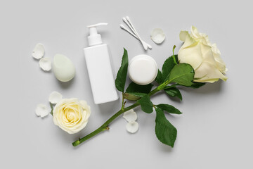 Beautiful white rose flowers with cosmetic products, sponge and cotton swabs on grey background