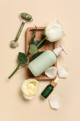 Beautiful white rose flowers with bottles of cosmetic products and jade roller on beige background