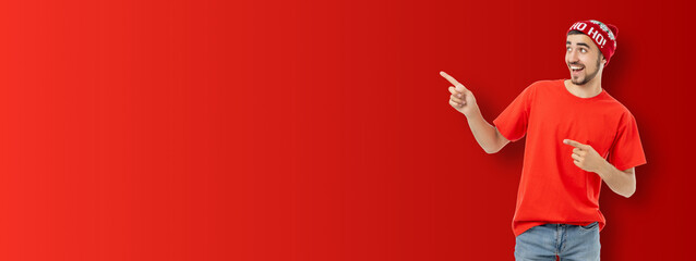 Man in red attire pointing cheerfully at a solid red backdrop