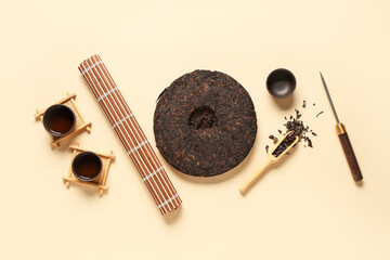 Composition with dry pressed puer tea, wicker mat, scoop and knife on beige background
