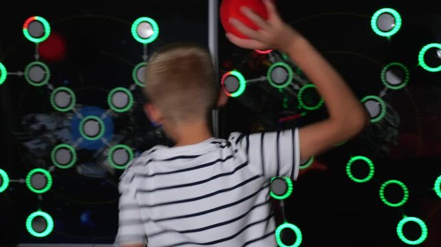Close-up of a boy throwing balls at glowing light bulbs in a modern play area. A game of marksmanship in a modern children's center.