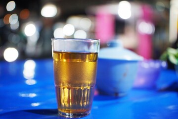 A glass of hot tea placed on a blue table at a night food stall.