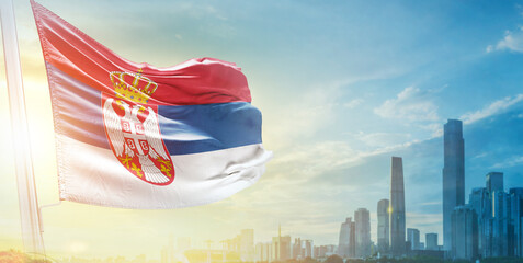 Serbia flag wavering in beautiful clouds with building skyline. The flag with drone shot in...