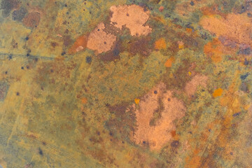 Top-down abstract aerial mosaic of a highly textured swampy wetland with patches of green, brown, and vivid rust-colored vegetation.