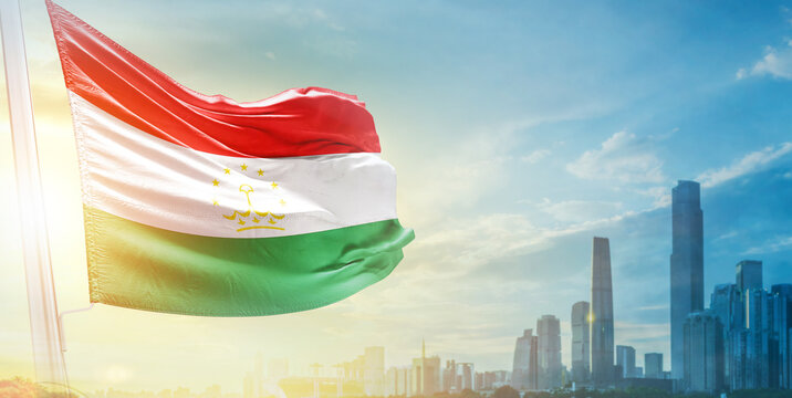 Tajikistan flag wavering in beautiful clouds with building skyline. The flag with drone shot in beautiful sky. Tajikistan national flag for independence day.