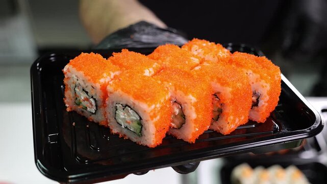 Close-up of a sushi chef serving a plate of delicious sushi in the restaurant's kitchen. The concept of catering and food delivery. - Powered by Adobe