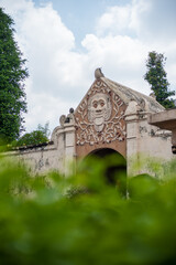 Ornate Stone Archway with Intricate Carved Face Amidst Lush Green Foliage.