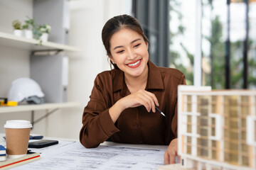 Young asian civil engineer studying a blueprint floor plan and working with documents, construction drawings and building models.