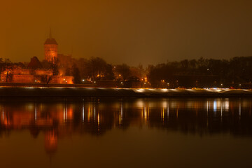 Toruń nocą, stare miasto nad rzeką Wisłą, światła odbijające się w wodzie. 