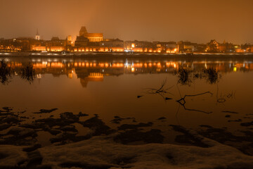 Toruń nocą, stare miasto nad rzeką Wisłą, światła odbijające się w wodzie. 