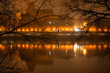 Toruń nocą, stare miasto nad rzeką Wisłą, światła odbijające się w wodzie. 