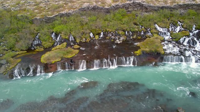 Scenic Hraunfossar water falls in Iceland countryside where water flows from under lava stones.