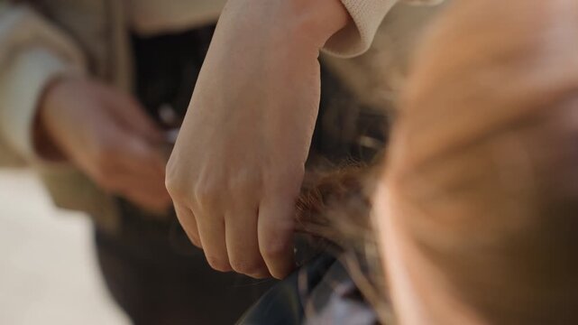 braiding vibrant red tresses slowly, sunlit fingers intertwine bright hair strands carefully, detailed shot of fingers gently braiding vividly colored hair with natural light accentuating motion