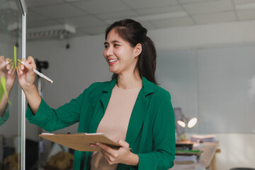 Smiling businesswoman writing ideas on glass whiteboard in office