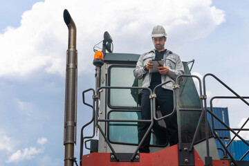 Engineer Using Digital Tablet to Check Inventory and Cargo Shipments on Reach Stacker, Logistics Professional in Safety Gear Standing on Truck, Overseeing Yard Management