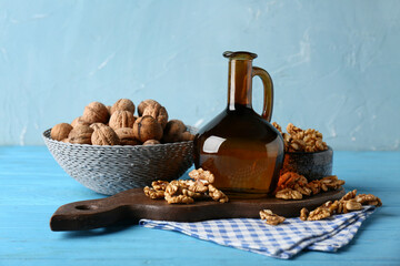 Bowls with tasty walnuts and jug of oil on wooden table against blue wall