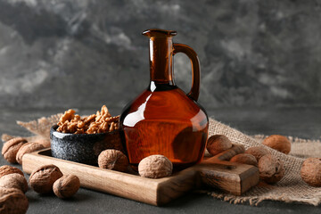 Bowl with tasty walnuts and jug of oil on grey grunge background