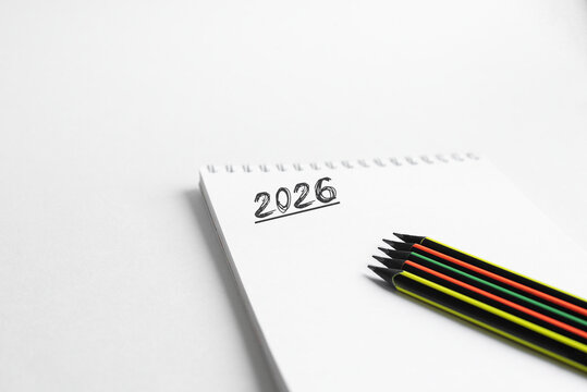 A blank notepad with the year 2026 written on it. Beside the notepad are colored pencils in red, yellow, green, and black.