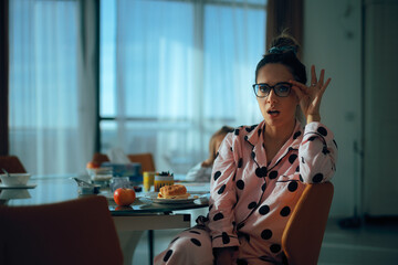 Surprised Housewife Wearing Glasses and Pajamas in her Living room. Funny expressive lady finding out something incredible holding her eyeglasses
