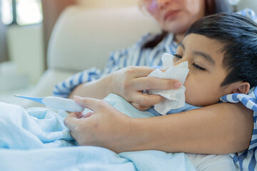 Obraz premium Sick child with high fever, mother holding thermometer and tissue for cleaning his nose