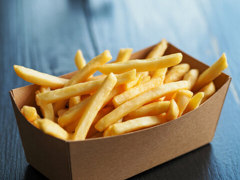 Golden French fries overflowing in eco-friendly container on dark table, perfect for fast food ads, restaurant menus, and tempting snack visuals