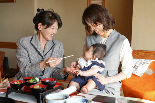 A woman is feeding a baby with chopsticks. The baby is wearing a blue dress