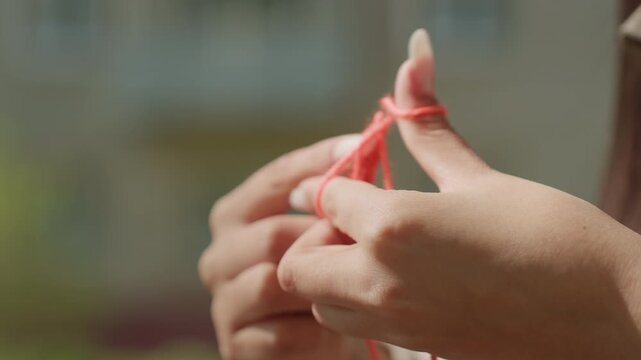 handmade yarn demonstration, bright urban setting with playful finger knitting tutorial demonstration, asian woman displaying intricate finger knitting process with red yarn in cityscape setting
