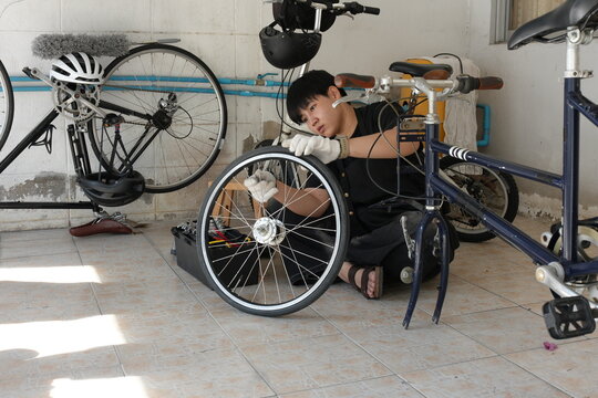 Authentic young tomboy repairing a flat bicycle tire in a garage. Independent female mechanic fixing a bike wheel with tools. DIY maintenance and empowerment concept. - Powered by Adobe