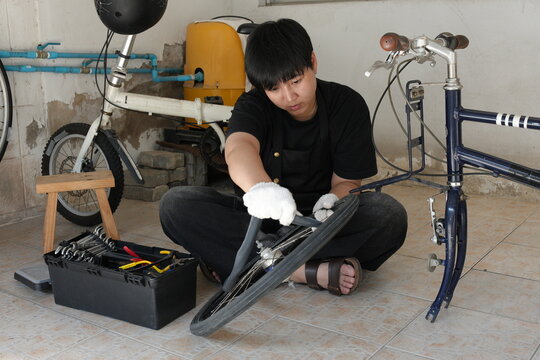 Authentic young tomboy repairing a flat bicycle tire in a garage. Independent female mechanic fixing a bike wheel with tools. DIY maintenance and empowerment concept. - Powered by Adobe