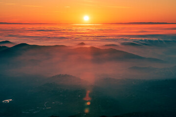 Sunset sun setting in clouds rolling over mountains range.