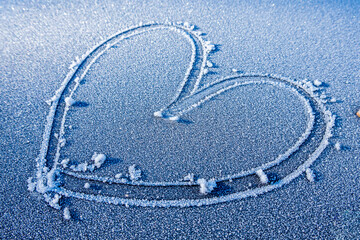 Heart shape drawn in frost on a cold winter morning with small stones on a gray surface