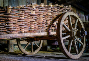 Vintage wooden cart with large wheels resting on a dusty floor in a rustic barn environment during the late afternoon light