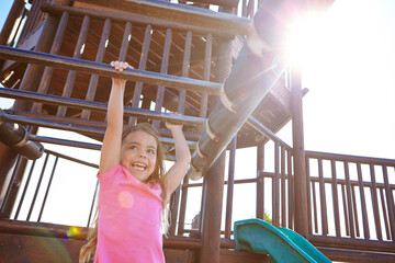 Happy girl, playing and hanging with monkey bars for playful childhood or fun outdoor summer. Kid, child or climbing with smile on jungle gym for youth, development or game at park or playground