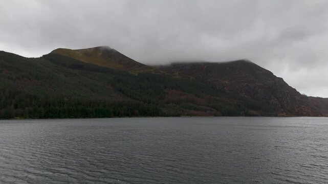 Aerial drone footage of scenic Lake Llyn Cwellyn surrounded by Snowdonia mountain ranges in Wales United Kingdom dramatic landscape with water reflection cloudy sky winter scenery