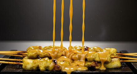 Delicious peanut sauce pouring over grilled chicken satay skewers. Appetizing Asian street food presentation.