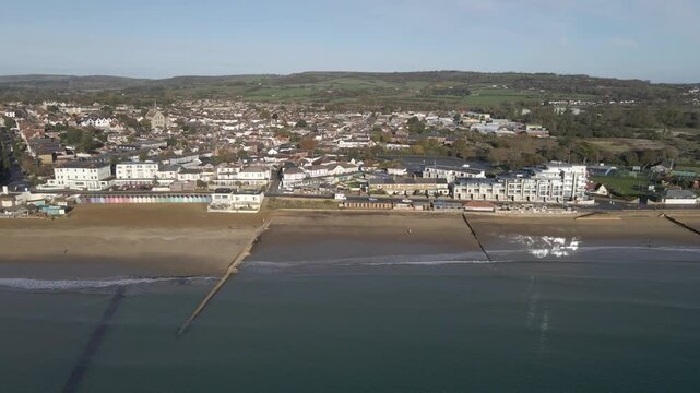 Aerial view of Sandown a seaside resort and civil parish on the south-east coast of the Isle of Wight, England. Drone moving to the left over the sea showing the yellow beach and the buildings.