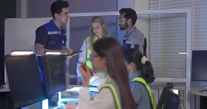 Engineers in high visibility vests collaborate in control room, reviewing digital site plans and dashboards during an operations and safety discussion. Coordination, monitoring, and incident readiness